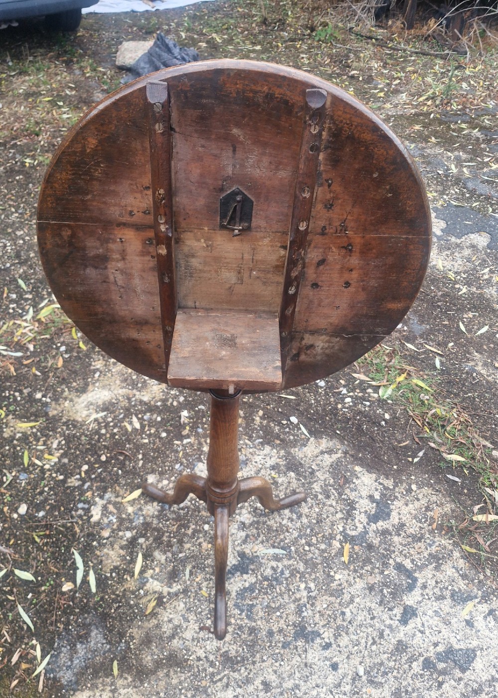 A late Georgian oak tripod table with a circular tilt-top surface positioned vertically, supported by a turned column and three cabriole legs. View V