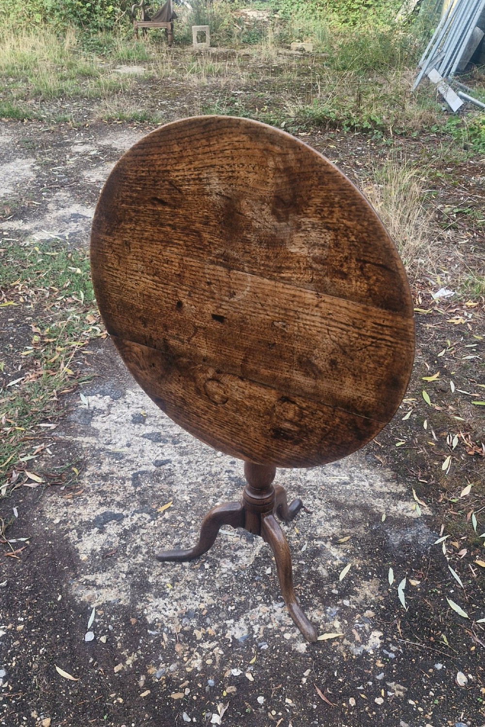 A late Georgian oak tripod table with a circular tilt-top surface positioned vertically, supported by a turned column and three cabriole legs. View VI