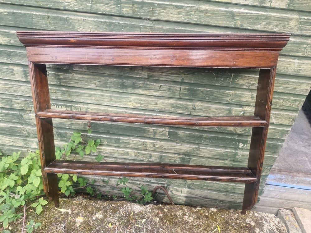 An antique dark oak wall-mounted plate rack featuring a moulded top cornice and two grooved display shelves.
