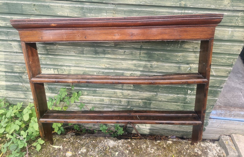An antique dark oak wall-mounted plate rack featuring a moulded top cornice and two grooved display shelves. View V