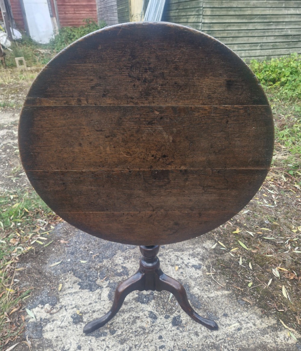 A dark oak 19th-century occasional table featuring a circular top tilted vertically on a turned pedestal with three cabriole legs.