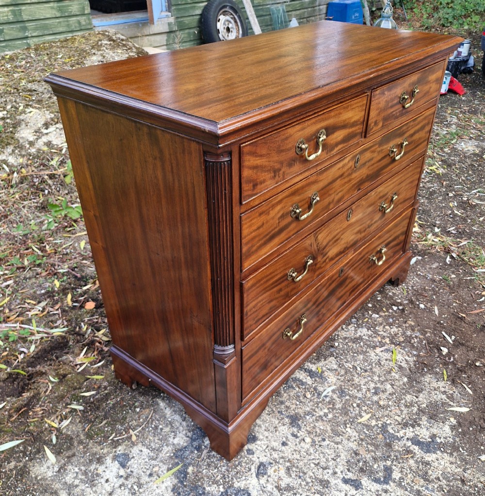 A Late Georgian mahogany chest of drawers featuring a two-over-three drawer configuration, fluted pilasters, bracket feet, and brass swan-neck handles. View X