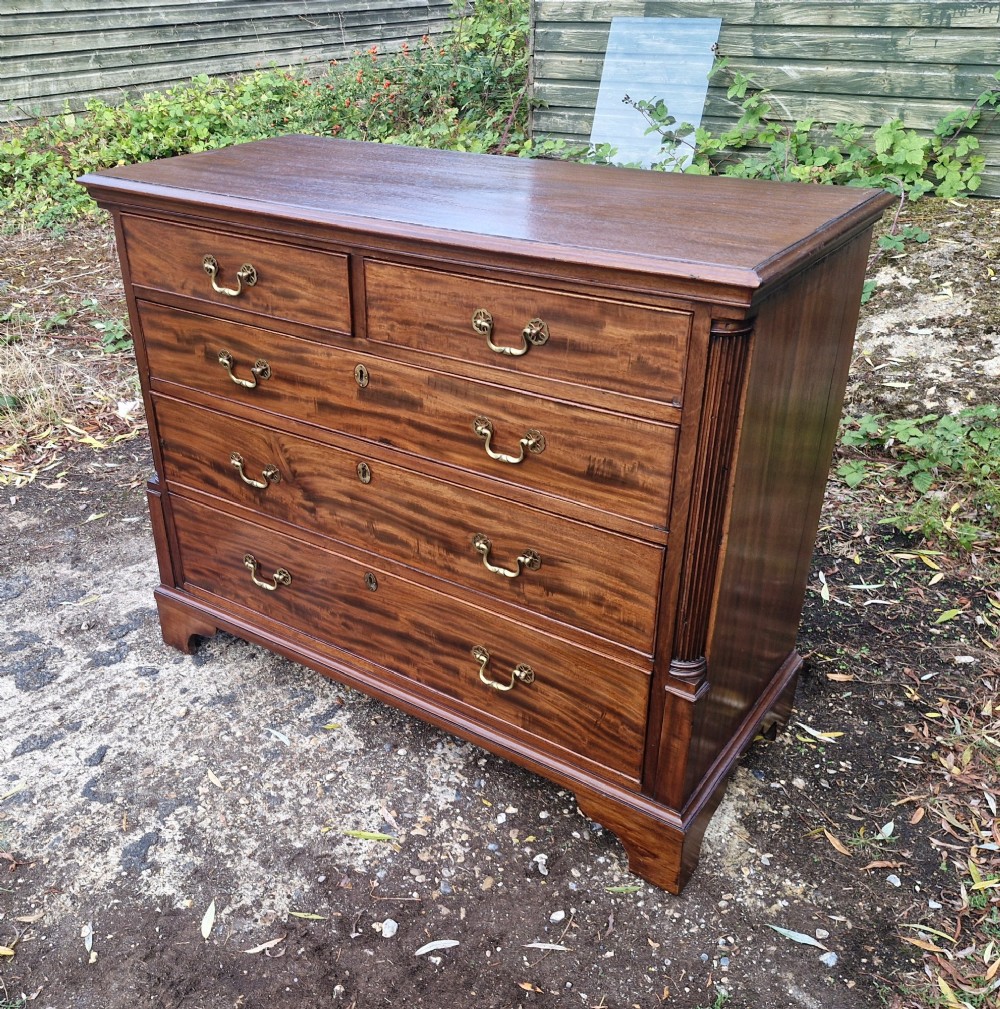 A Late Georgian mahogany chest of drawers featuring a two-over-three drawer configuration, fluted pilasters, bracket feet, and brass swan-neck handles. View XI