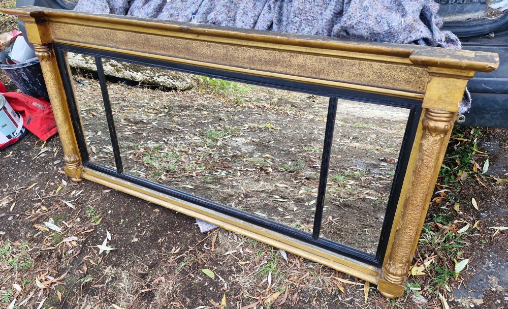 A Regency period horizontal tripartite overmantel mirror featuring a gilded architectural frame with classical fluted pilasters and an ebonised inner slip dividing three glass panels.