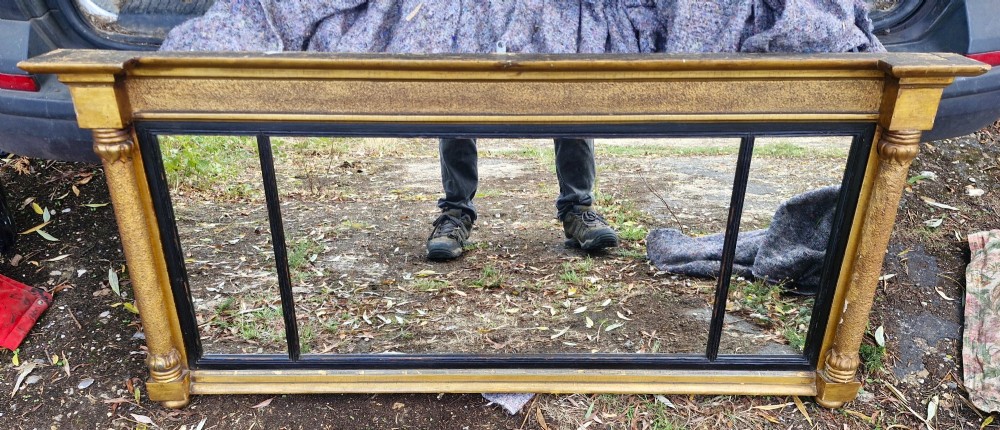 A Regency period horizontal tripartite overmantel mirror featuring a gilded architectural frame with classical fluted pilasters and an ebonised inner slip dividing three glass panels. View XI