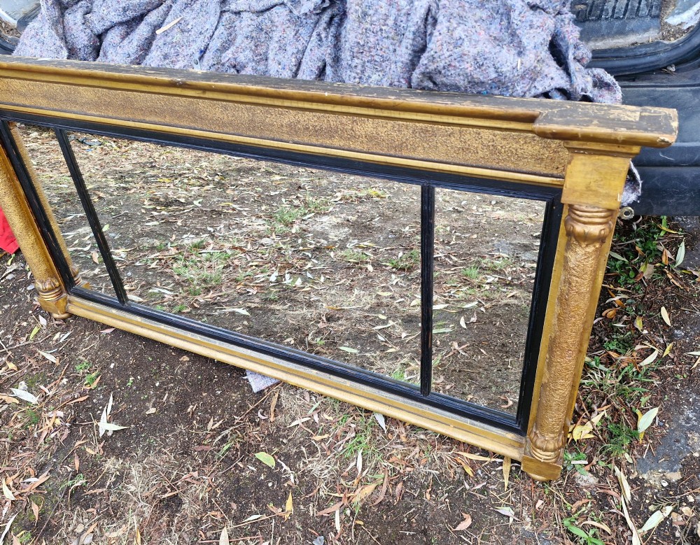 A Regency period horizontal tripartite overmantel mirror featuring a gilded architectural frame with classical fluted pilasters and an ebonised inner slip dividing three glass panels. View XII