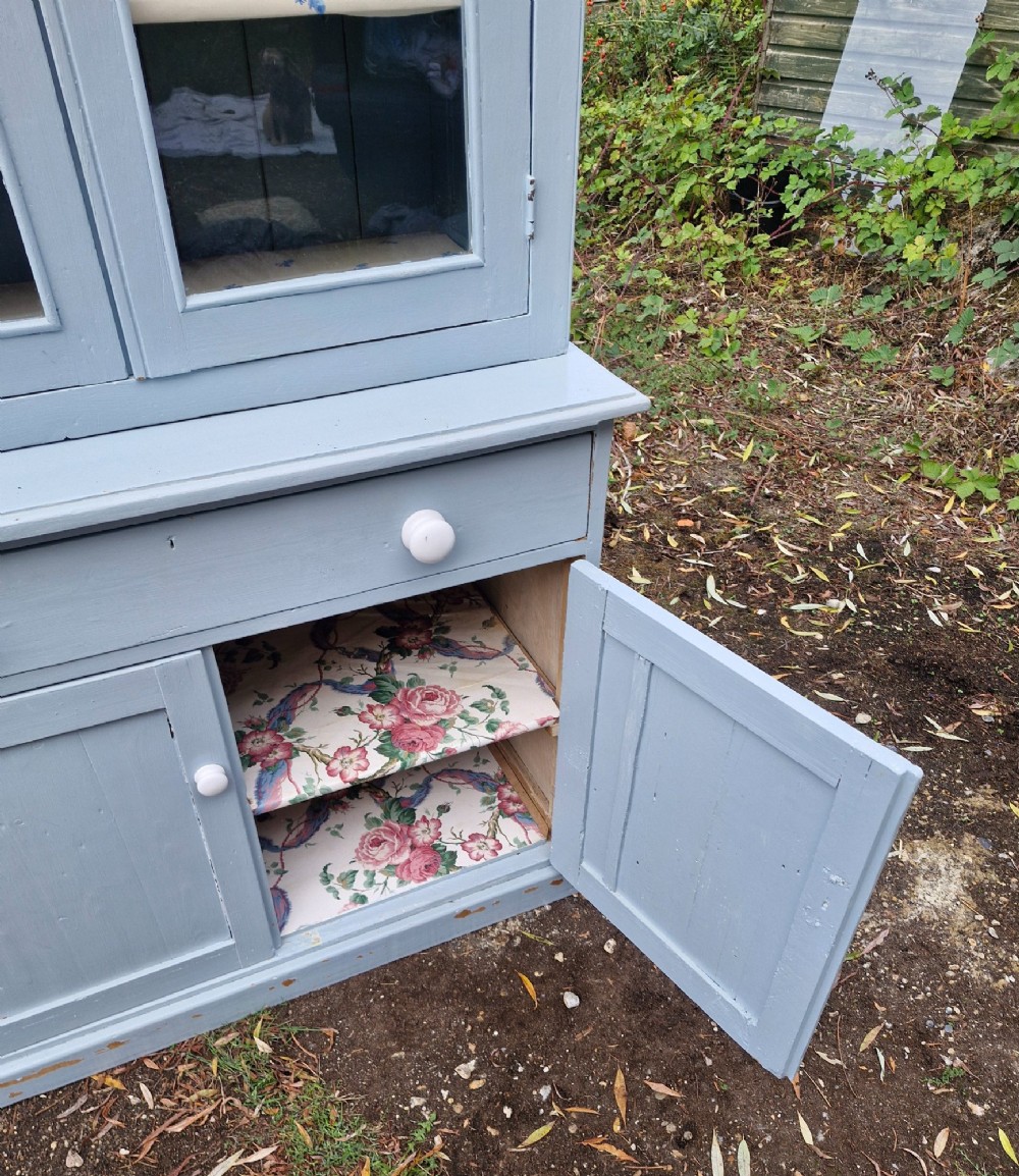A freestanding two-part slate blue painted pine kitchen cupboard featuring an upper glazed display cabinet with two doors above a lower base with a drawer and panelled doors. View II