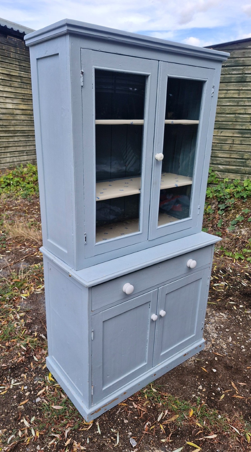 A freestanding two-part slate blue painted pine kitchen cupboard featuring an upper glazed display cabinet with two doors above a lower base with a drawer and panelled doors. View III