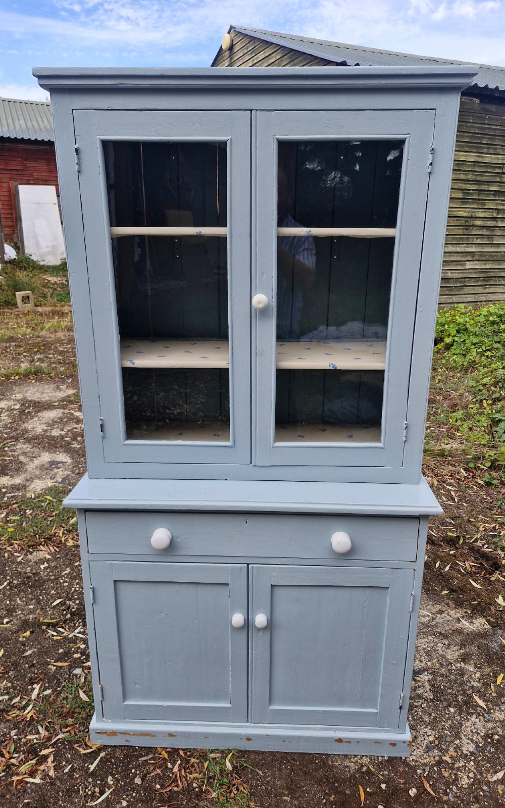 A freestanding two-part slate blue painted pine kitchen cupboard featuring an upper glazed display cabinet with two doors above a lower base with a drawer and panelled doors. View V
