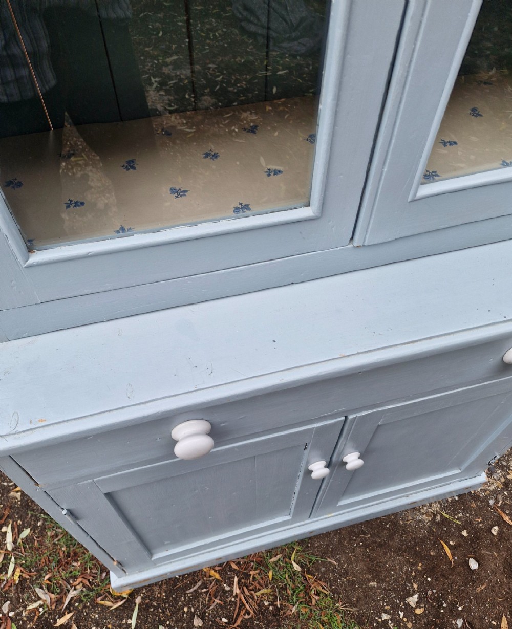 A freestanding two-part slate blue painted pine kitchen cupboard featuring an upper glazed display cabinet with two doors above a lower base with a drawer and panelled doors. View VI