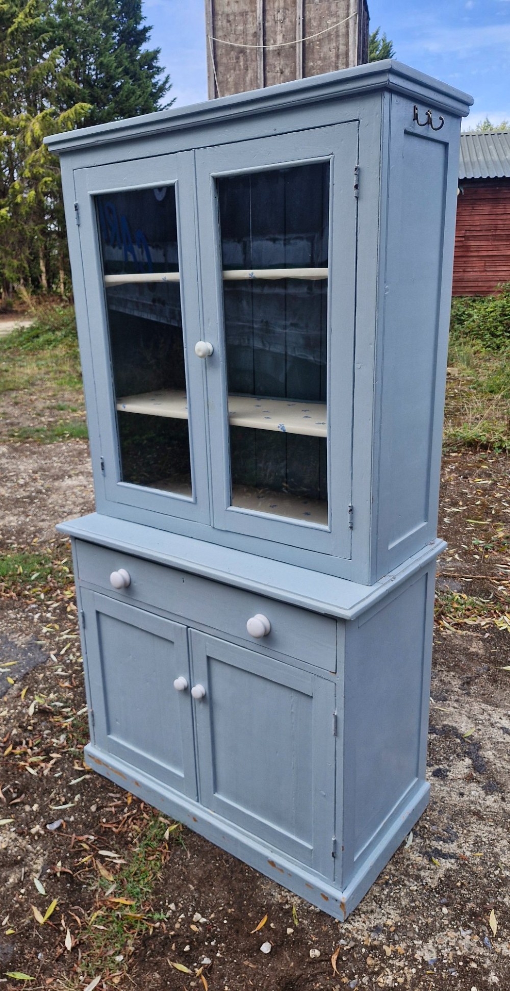 A freestanding two-part slate blue painted pine kitchen cupboard featuring an upper glazed display cabinet with two doors above a lower base with a drawer and panelled doors. View VII