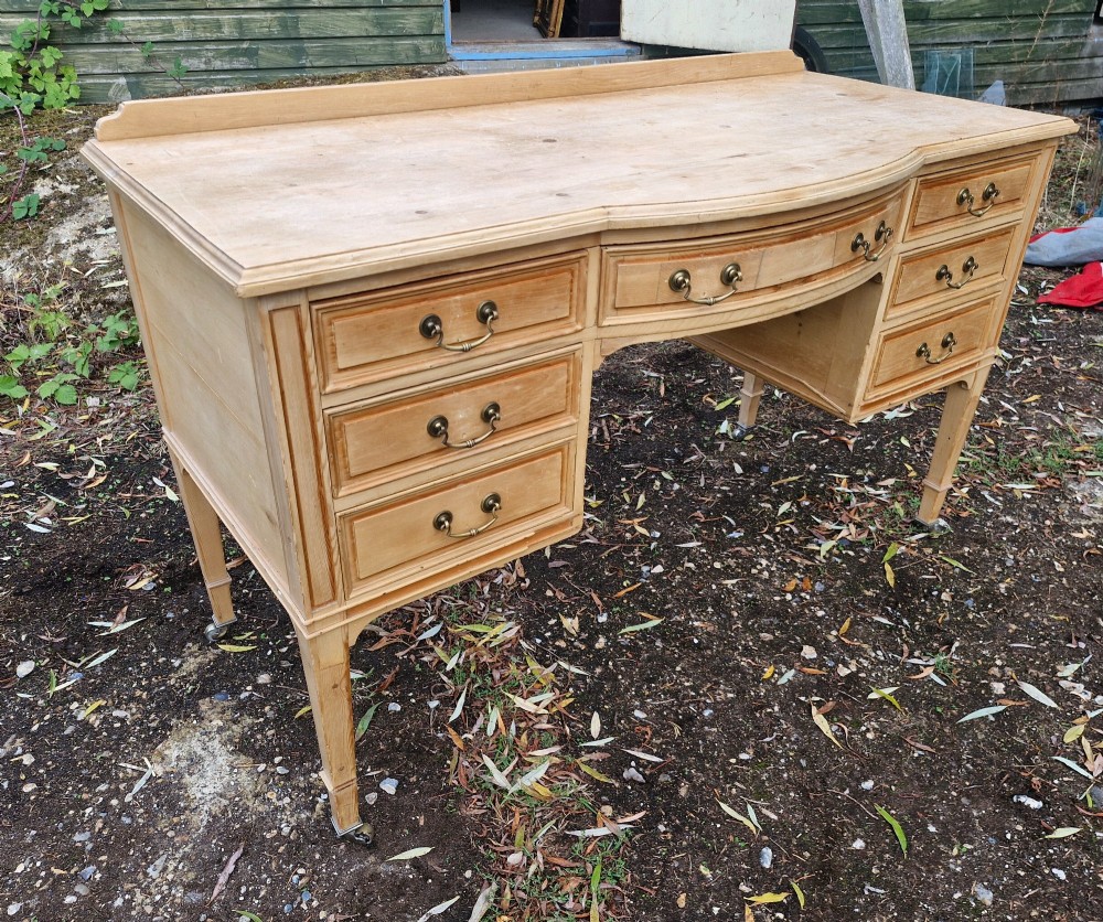 An Edwardian pine kneehole writing table featuring seven drawers with brass handles, a curved central drawer, and tapered legs on castors. View III