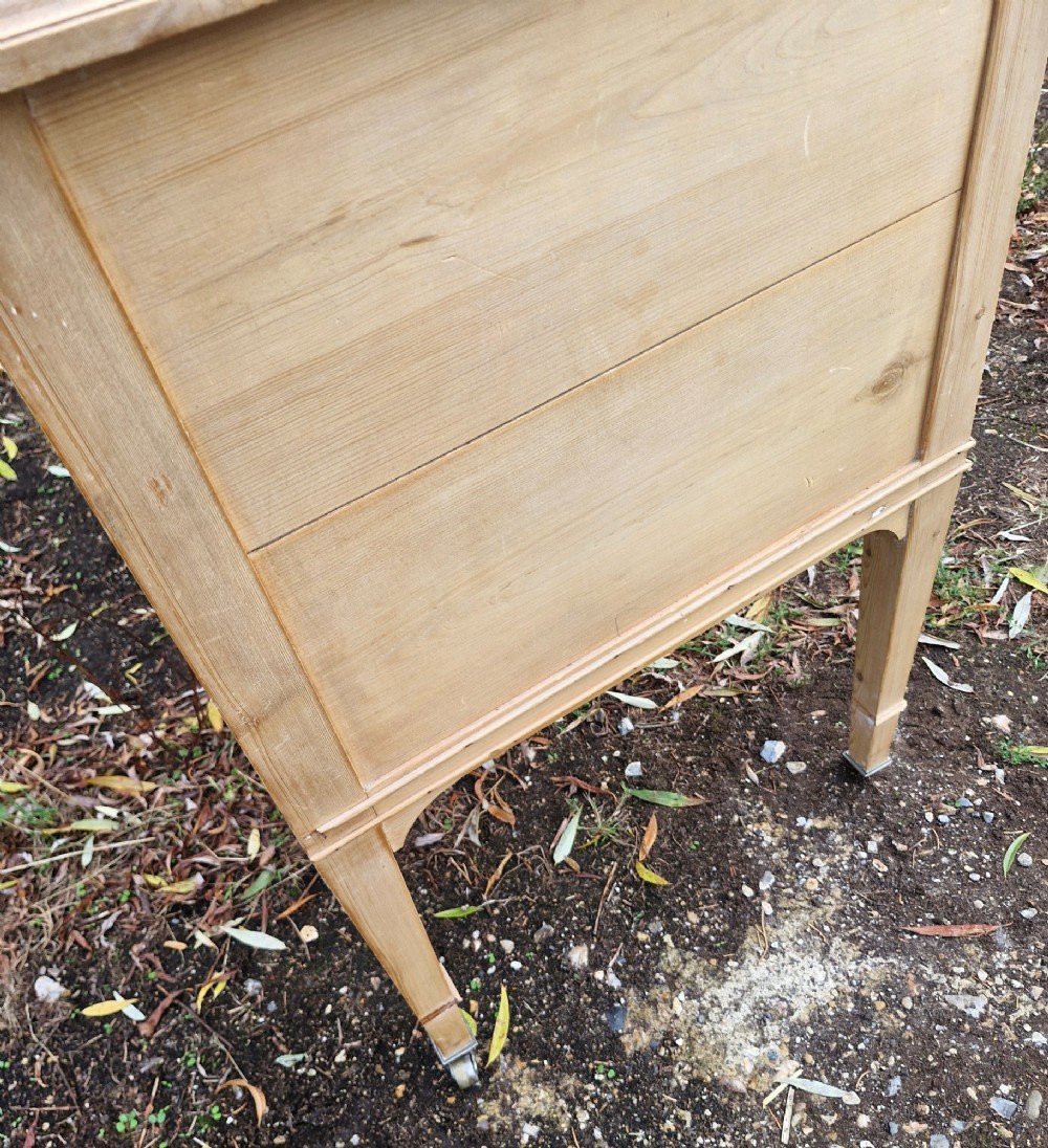An Edwardian pine kneehole writing table featuring seven drawers with brass handles, a curved central drawer, and tapered legs on castors. View IV