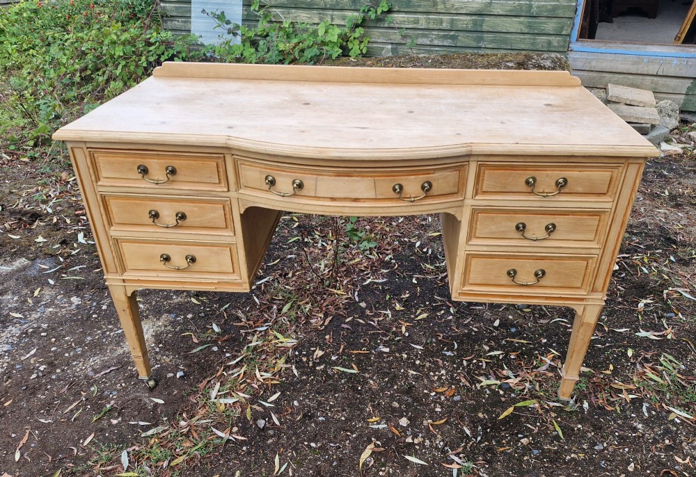 An Edwardian pine kneehole writing table featuring seven drawers with brass handles, a curved central drawer, and tapered legs on castors. View VII
