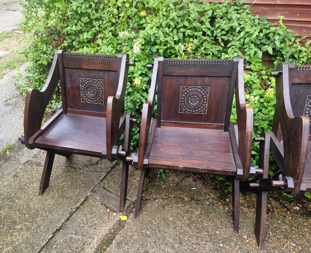 A set of four dark brown carved oak Glastonbury armchairs with X-frame legs and circular rosette backrests. View V