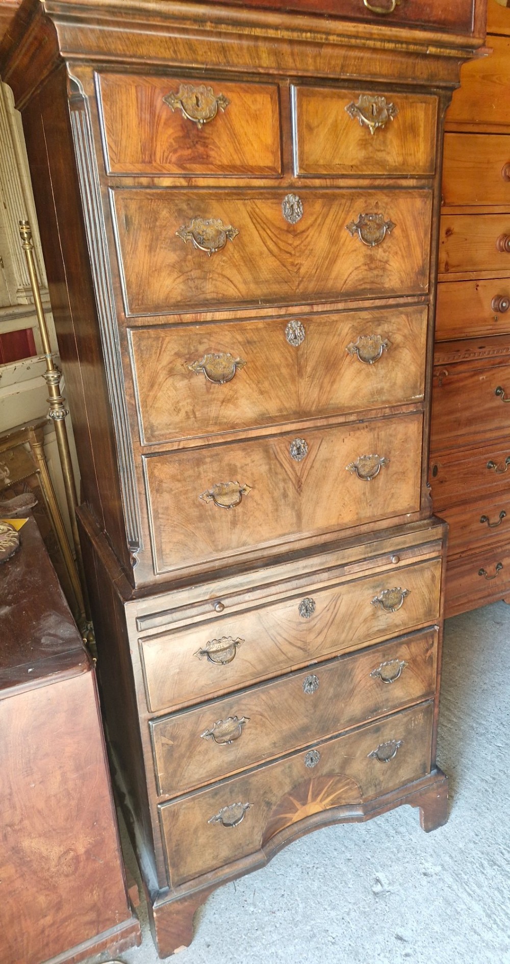 An early 20th century walnut chest on chest featuring brass drop handles, a pull-out brushing slide, and an inlaid sunburst motif on the lower drawer. View II