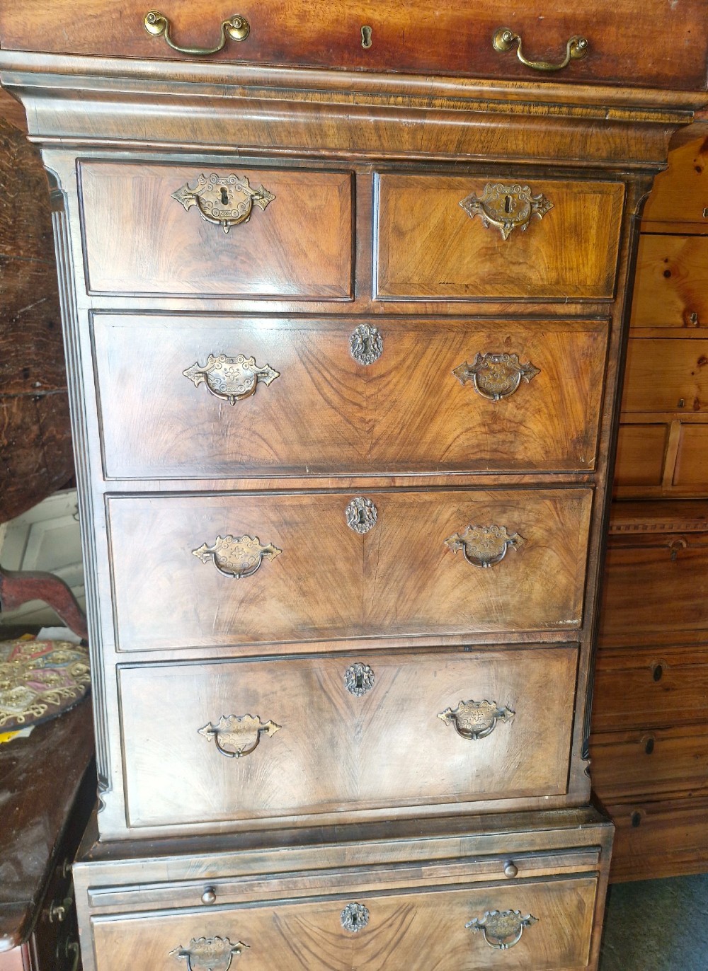An early 20th century walnut chest on chest featuring brass drop handles, a pull-out brushing slide, and an inlaid sunburst motif on the lower drawer. View III