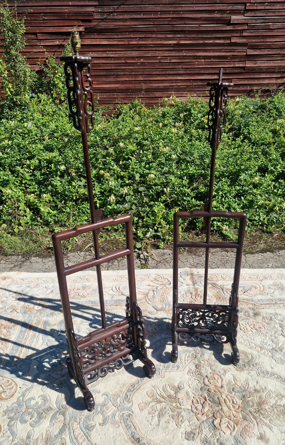 A pair of dark carved hardwood Chinese adjustable standard lamps featuring openwork bases and slender vertical shafts.