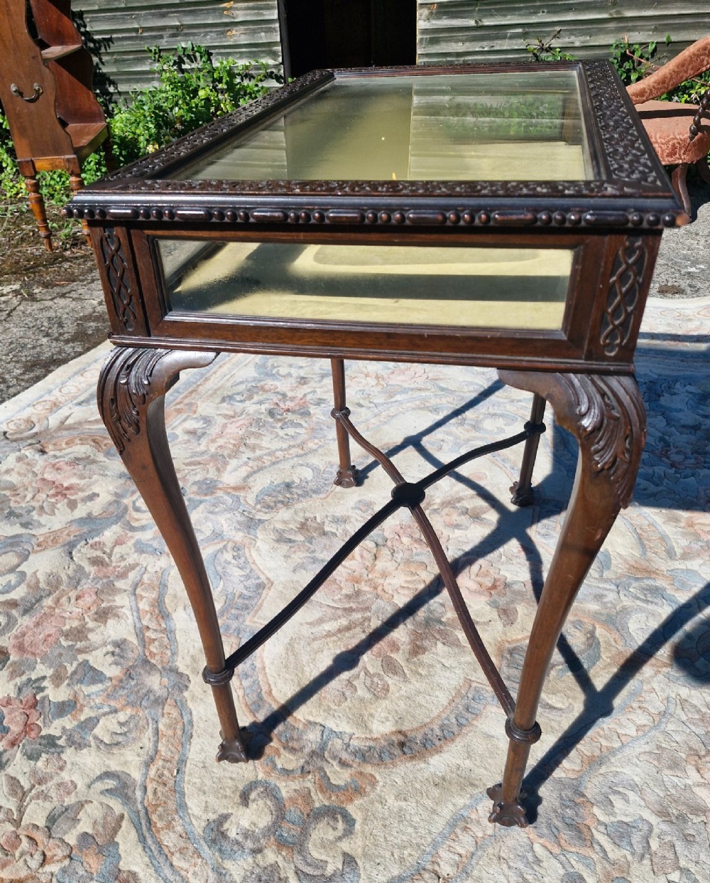An Edwardian carved mahogany bijouterie table with glass display panels, cabriole legs, and an X-frame stretcher. View II
