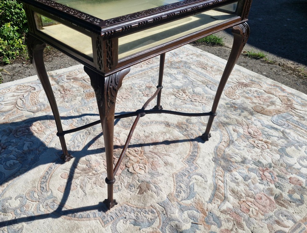 An Edwardian carved mahogany bijouterie table with glass display panels, cabriole legs, and an X-frame stretcher. View III