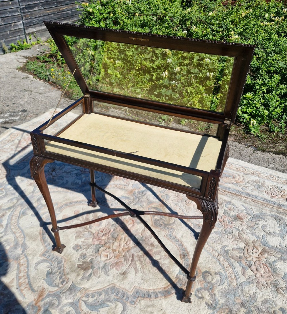 An Edwardian carved mahogany bijouterie table with glass display panels, cabriole legs, and an X-frame stretcher. View IV