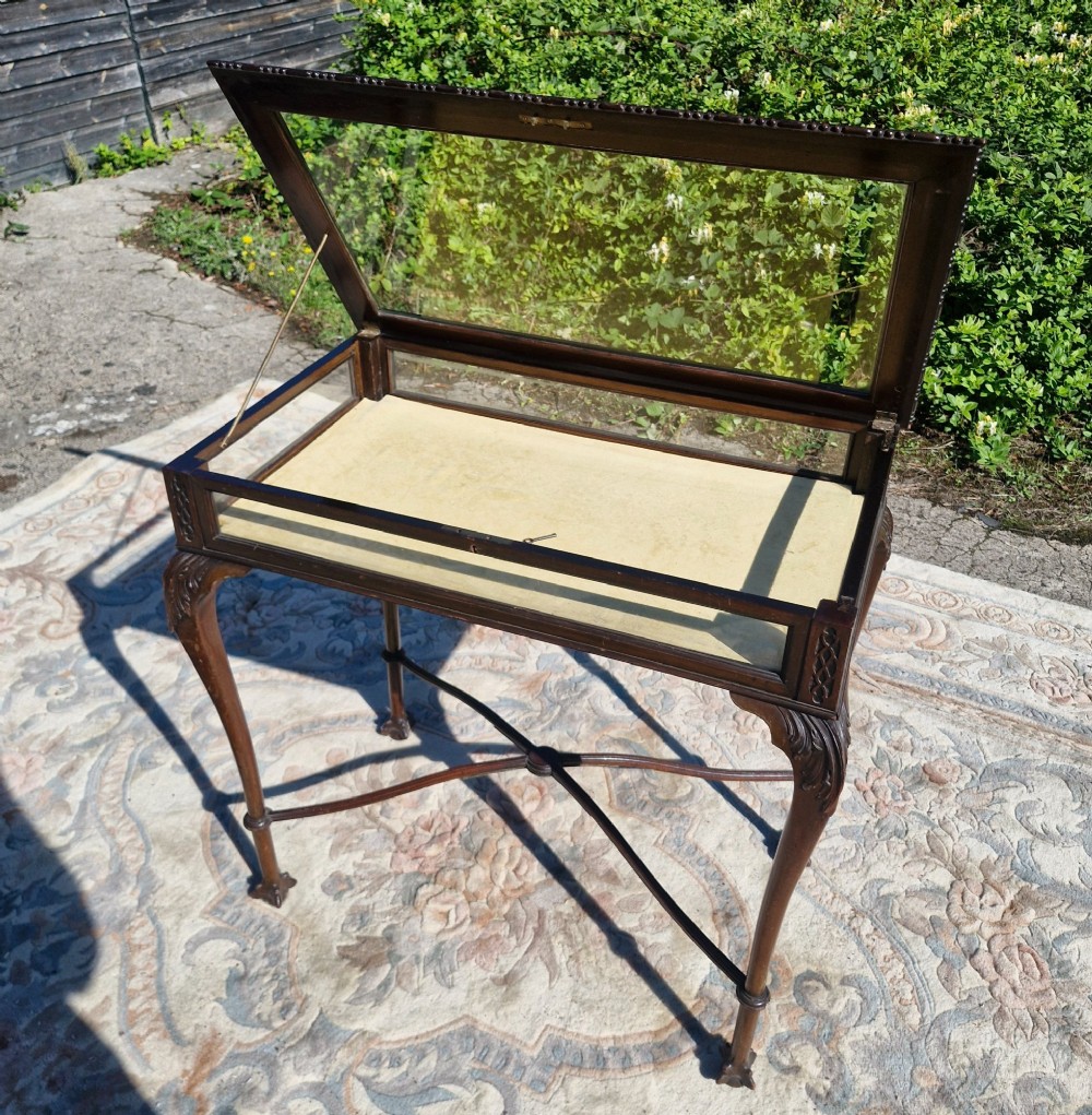 An Edwardian carved mahogany bijouterie table with glass display panels, cabriole legs, and an X-frame stretcher. View V