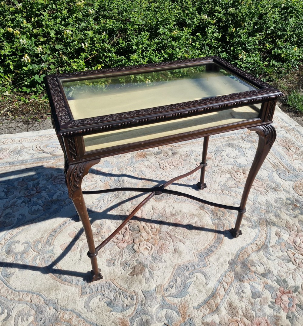 An Edwardian carved mahogany bijouterie table with glass display panels, cabriole legs, and an X-frame stretcher. View VI