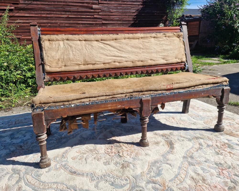 A Victorian mahogany hall bench featuring a padded backrest and seat upholstered in hessian cloth, supported by turned front legs and carved wooden trim.