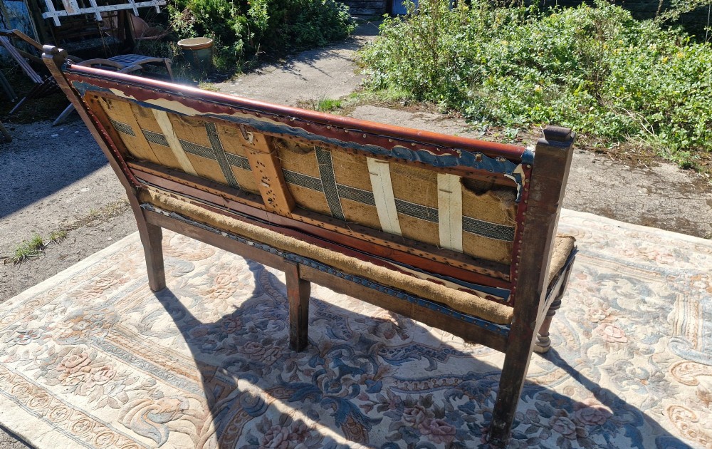 A Victorian mahogany hall bench featuring a padded backrest and seat upholstered in hessian cloth, supported by turned front legs and carved wooden trim. View IV
