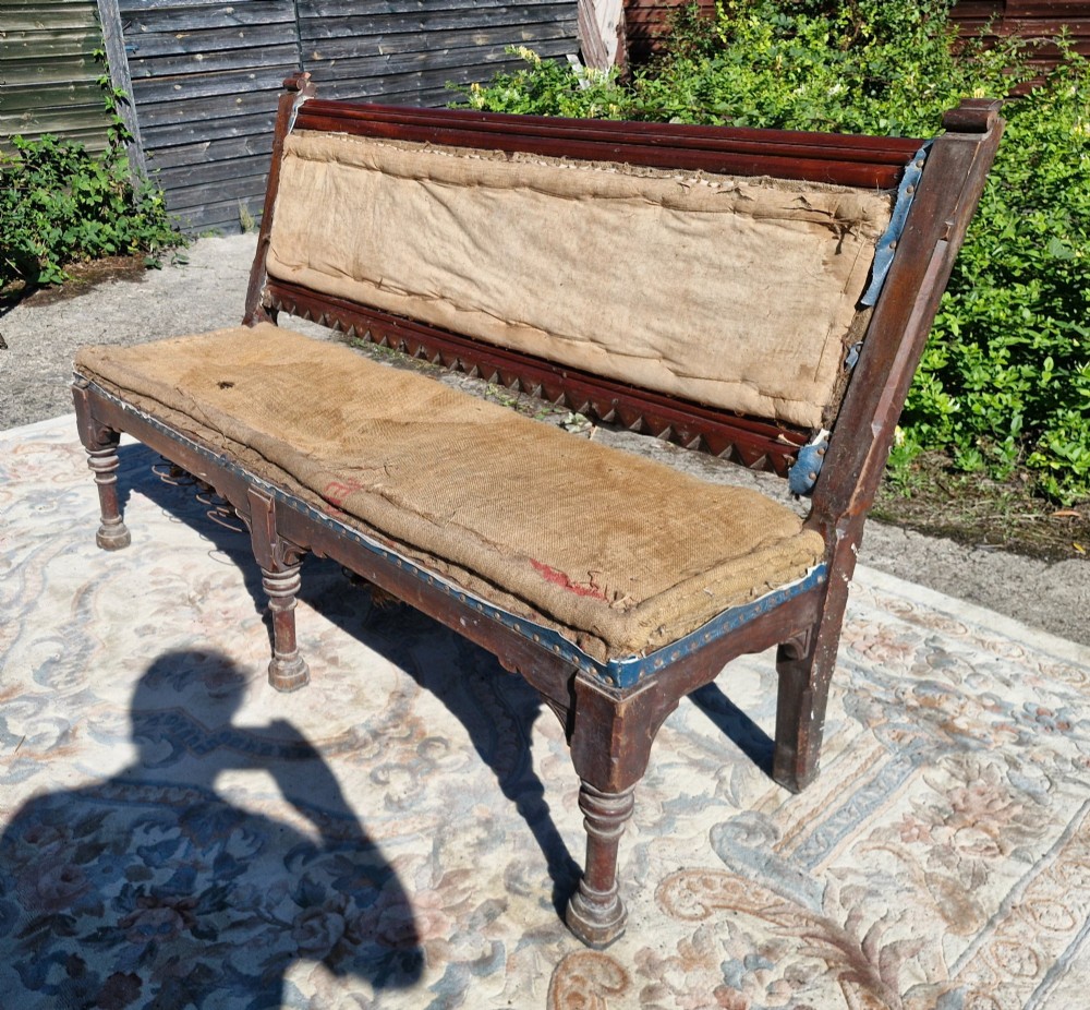 A Victorian mahogany hall bench featuring a padded backrest and seat upholstered in hessian cloth, supported by turned front legs and carved wooden trim. View V