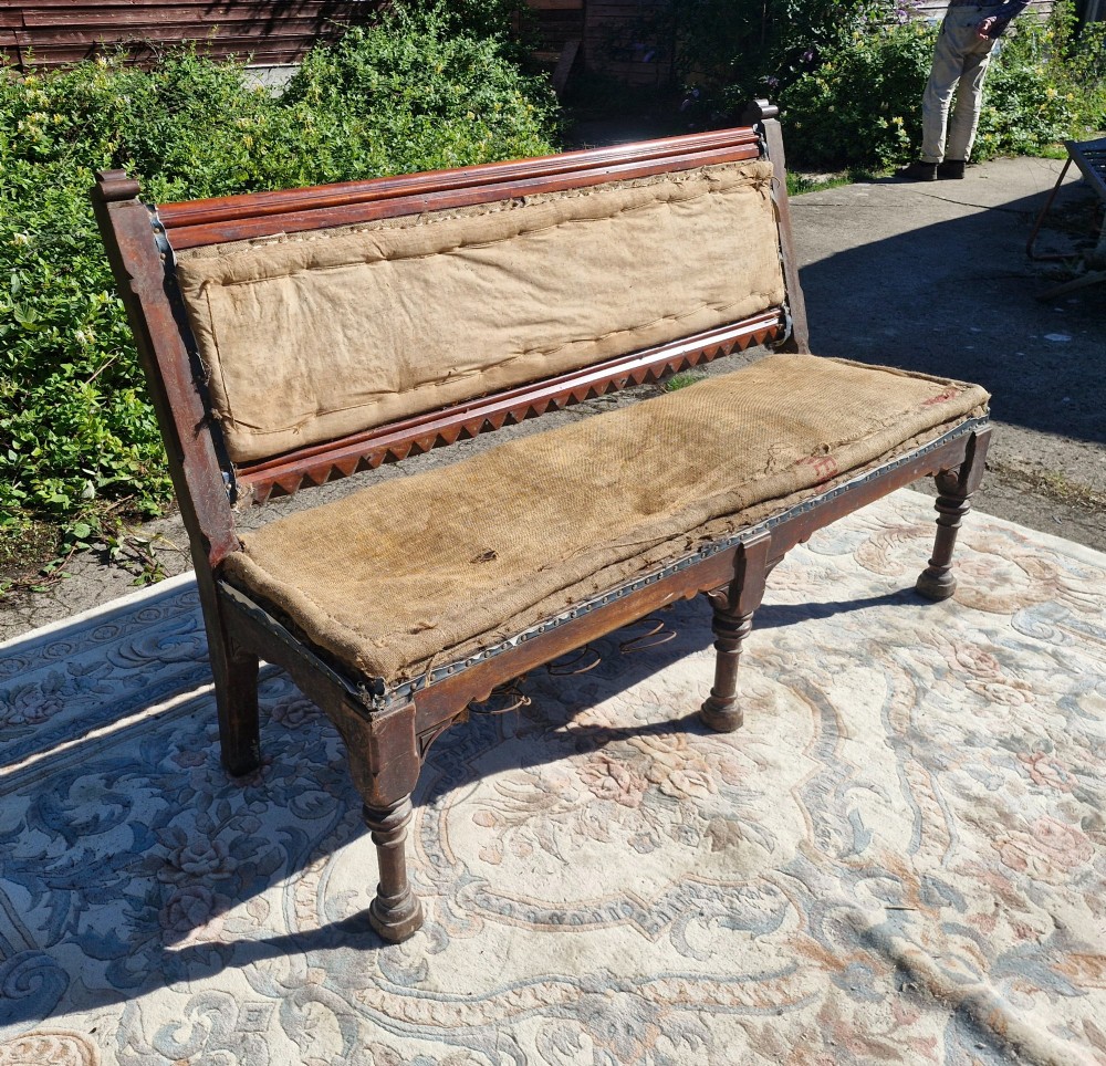 A Victorian mahogany hall bench featuring a padded backrest and seat upholstered in hessian cloth, supported by turned front legs and carved wooden trim. View VI