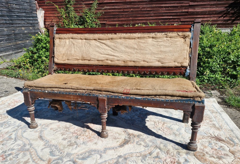 A Victorian mahogany hall bench featuring a padded backrest and seat upholstered in hessian cloth, supported by turned front legs and carved wooden trim. View VII