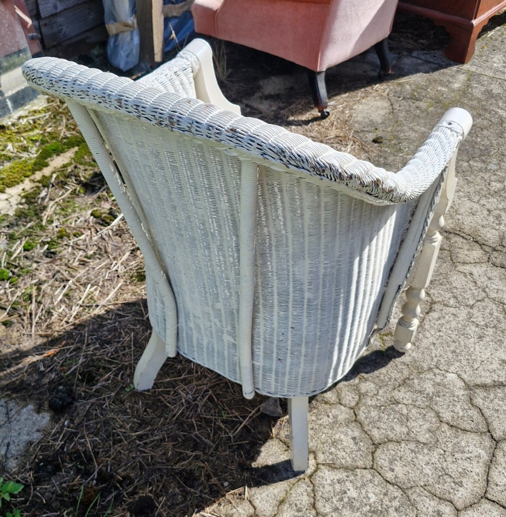 A painted off-white woven Lloyd Loom armchair featuring turned front legs, wooden arm supports, and a removable patterned fabric seat cushion. View II