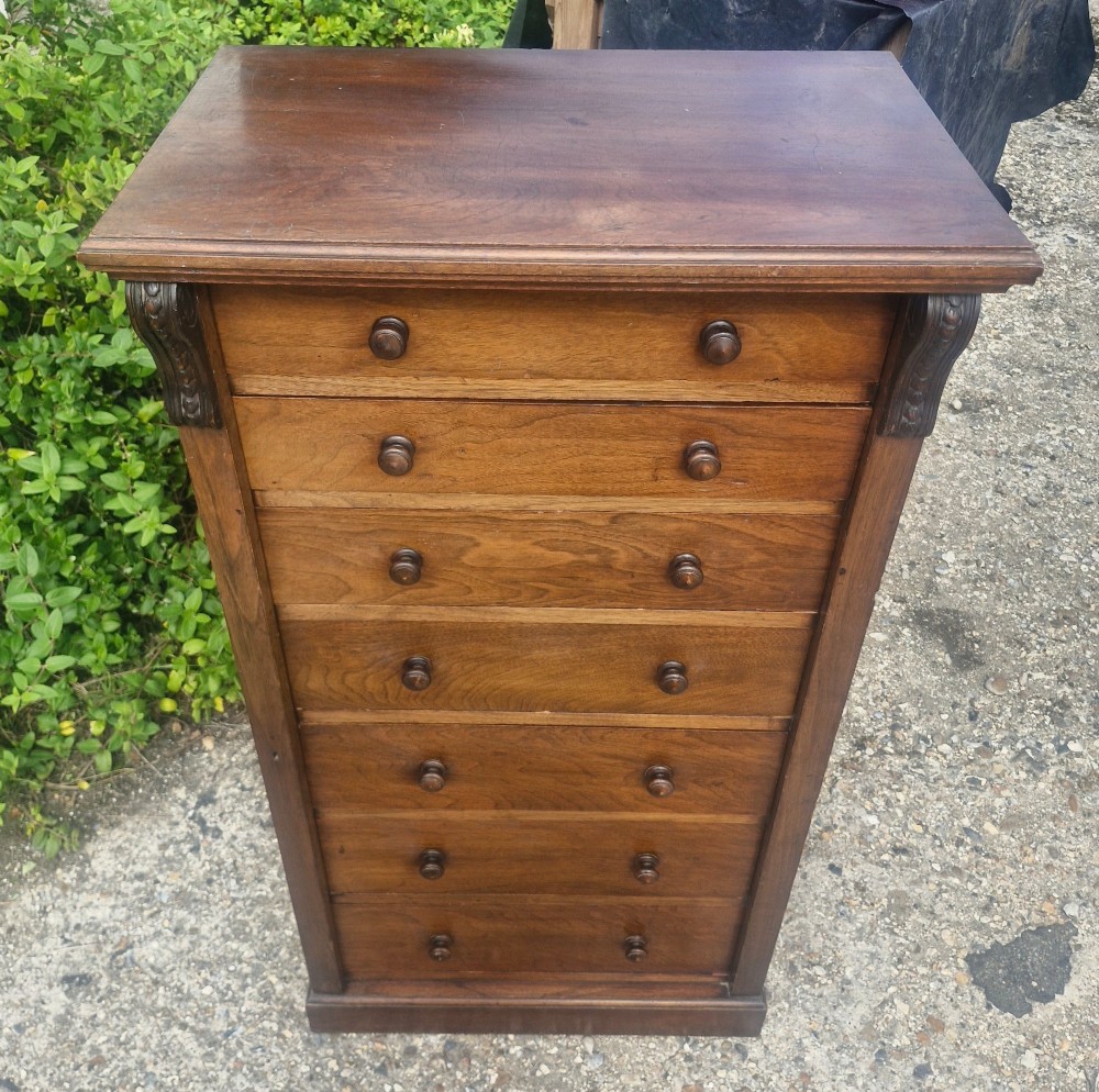A tall, narrow mahogany Wellington chest with seven drawers featuring turned wooden knobs and carved corbels. View III