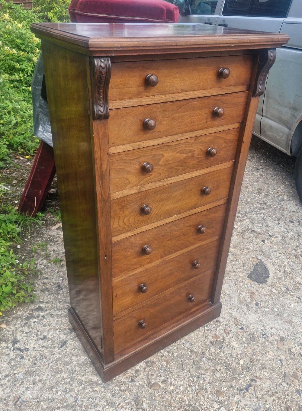 A tall, narrow mahogany Wellington chest with seven drawers featuring turned wooden knobs and carved corbels. View IV