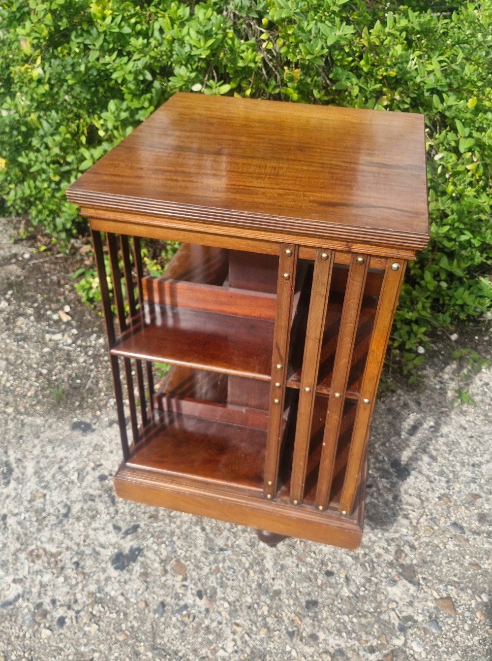 A late Victorian mahogany revolving bookcase featuring two square open tiers with vertical slatted sides fixed by brass studs.
