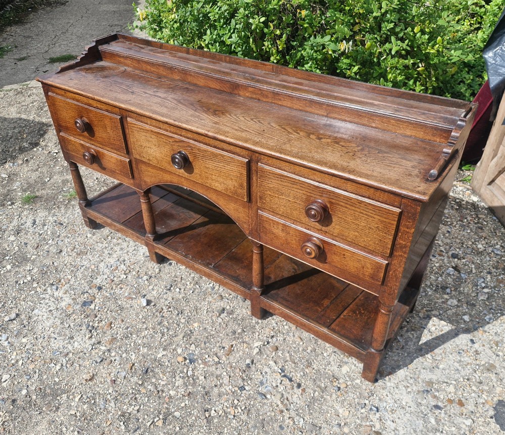 A Regency two-part Welsh oak dresser featuring an upper open three-shelf plate rack above five drawers, an arched central apron, turned supports, and a lower pot board shelf. View III