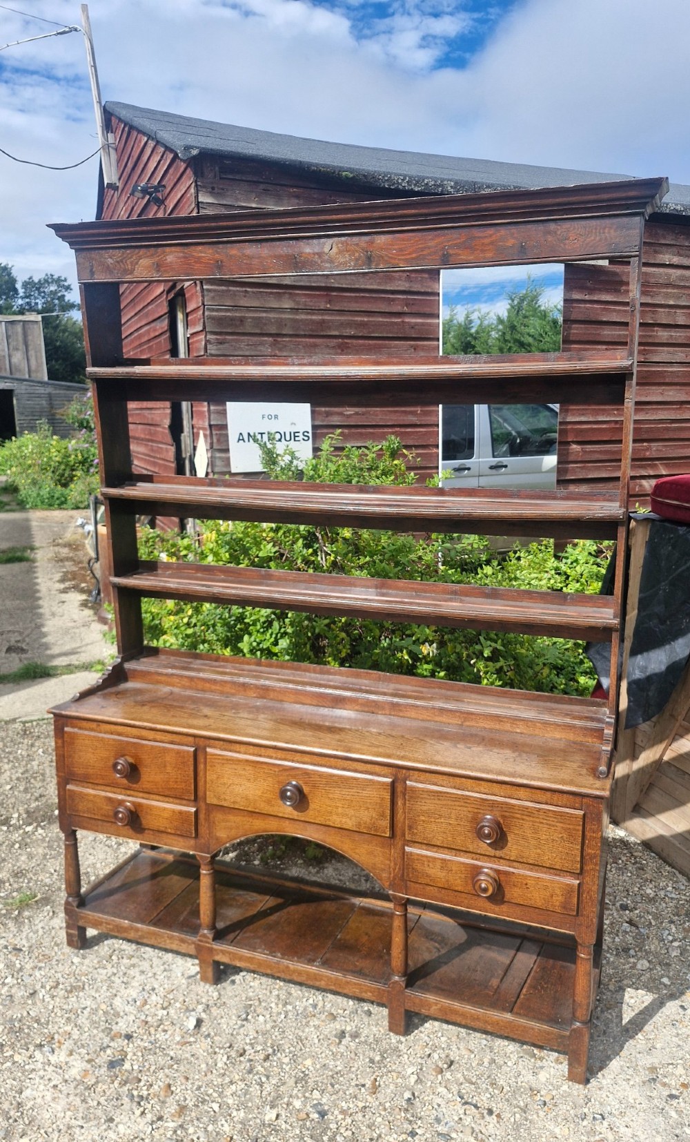 A Regency two-part Welsh oak dresser featuring an upper open three-shelf plate rack above five drawers, an arched central apron, turned supports, and a lower pot board shelf. View IV