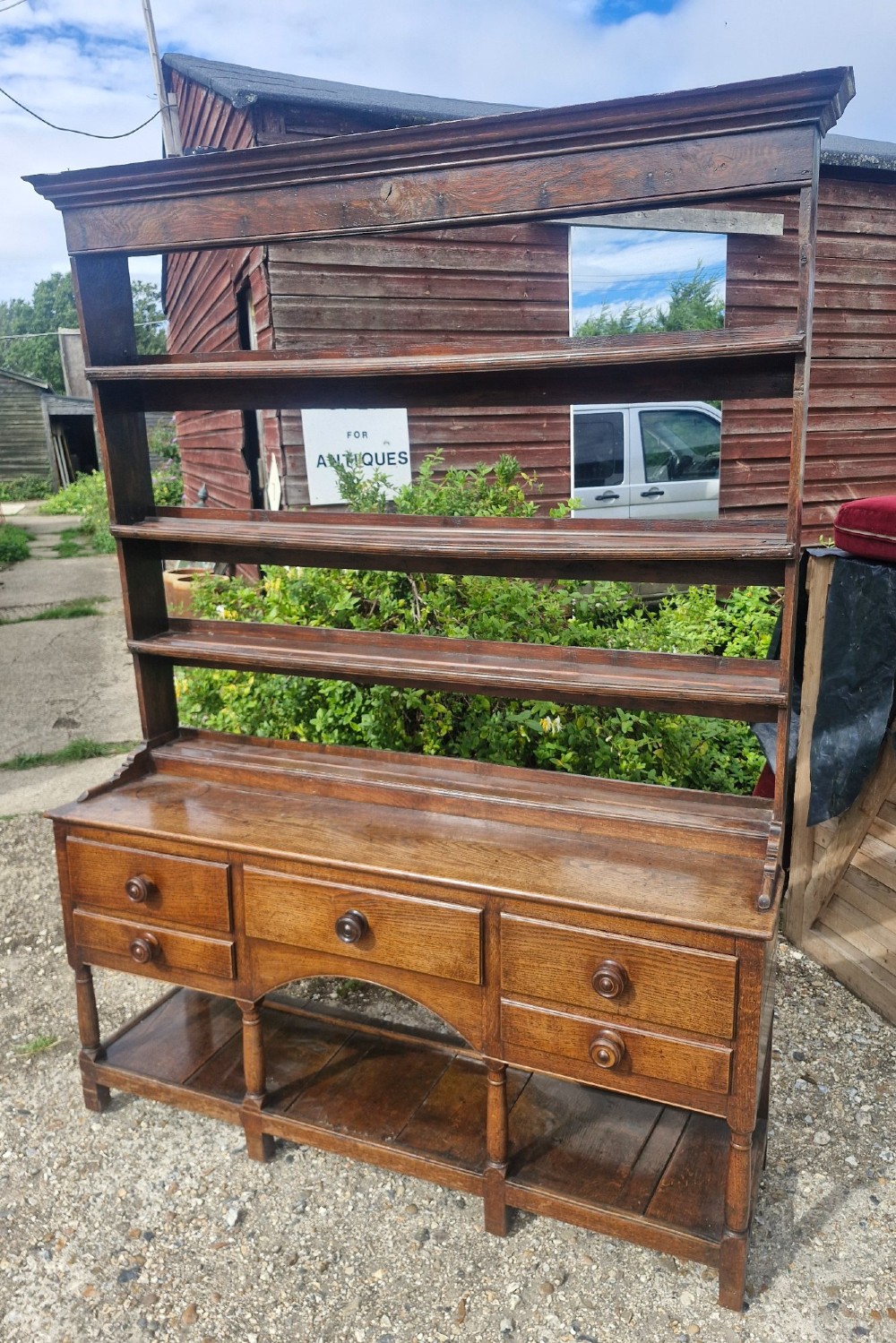 A Regency two-part Welsh oak dresser featuring an upper open three-shelf plate rack above five drawers, an arched central apron, turned supports, and a lower pot board shelf. View VI
