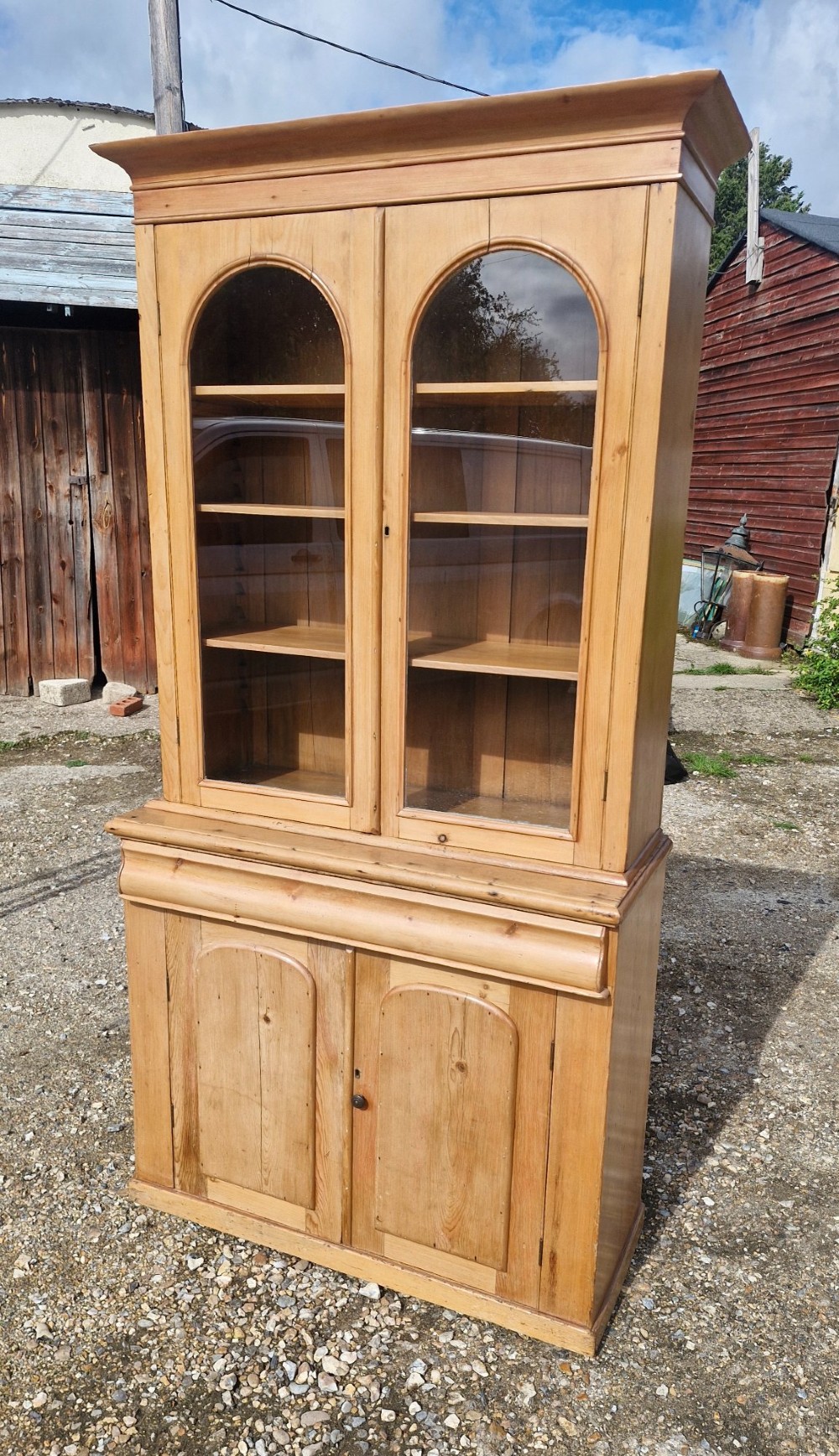 An early Victorian pine glazed bookcase featuring arched glass upper doors above a lower two-door cupboard base. View VI