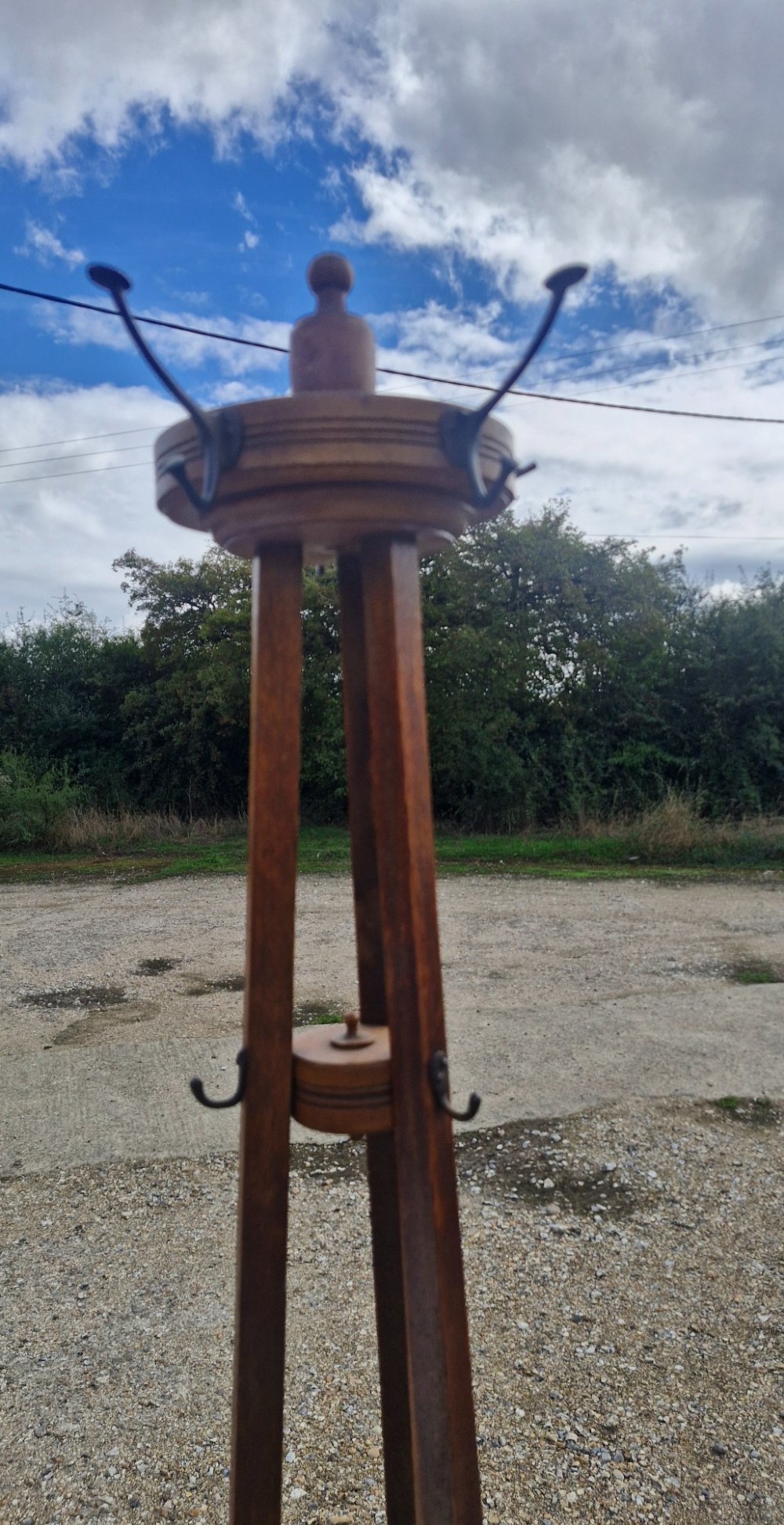 An Edwardian freestanding oak hat and coat stand featuring a revolving circular top with metal hooks, tapered tripod legs, and a bottom umbrella drip tray. View IV