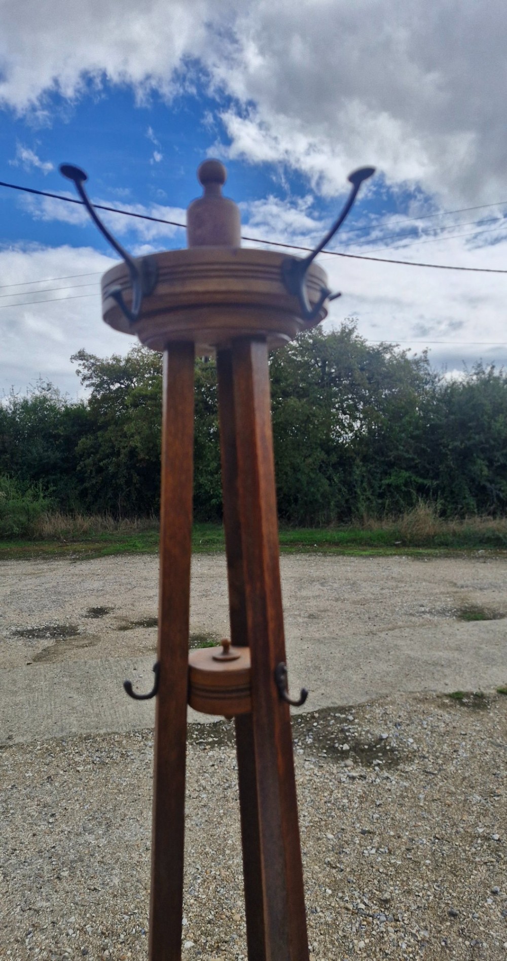 An Edwardian freestanding oak hat and coat stand featuring a revolving circular top with metal hooks, tapered tripod legs, and a bottom umbrella drip tray. View V