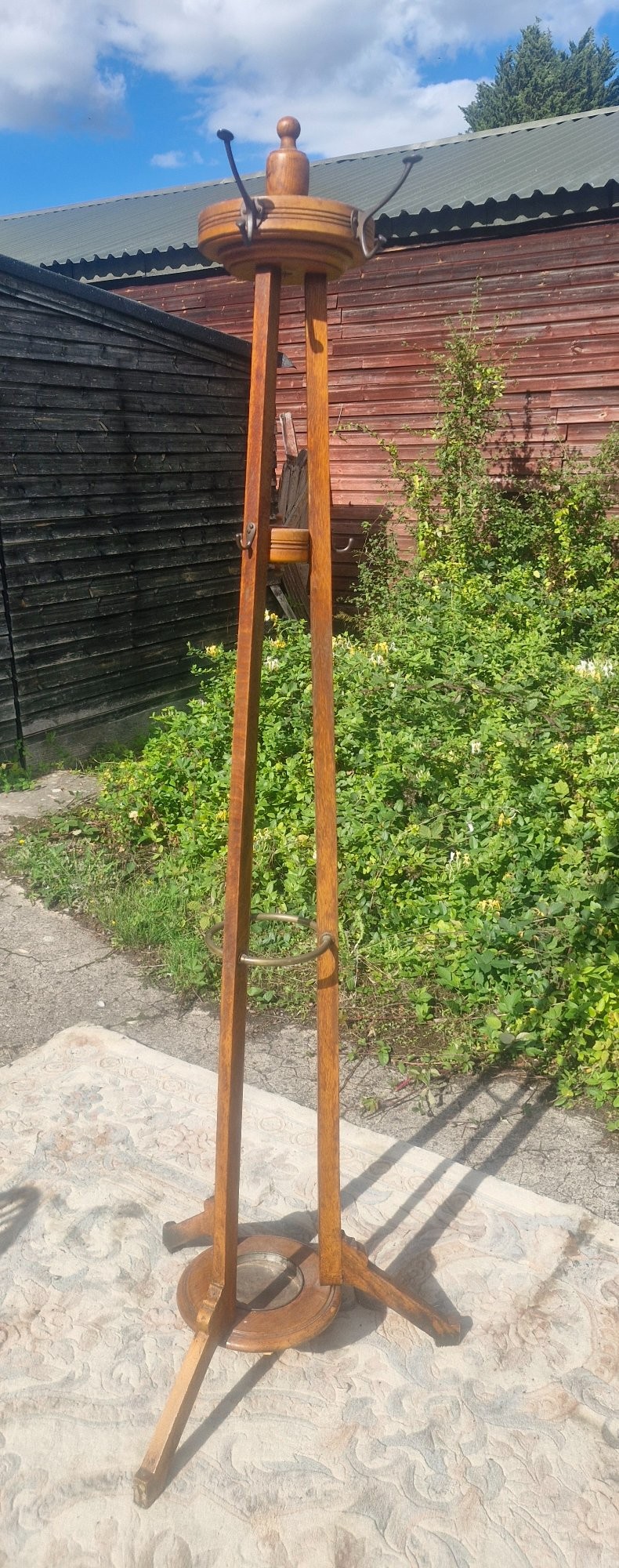An Edwardian freestanding oak hat and coat stand featuring a revolving circular top with metal hooks, tapered tripod legs, and a bottom umbrella drip tray. View VII