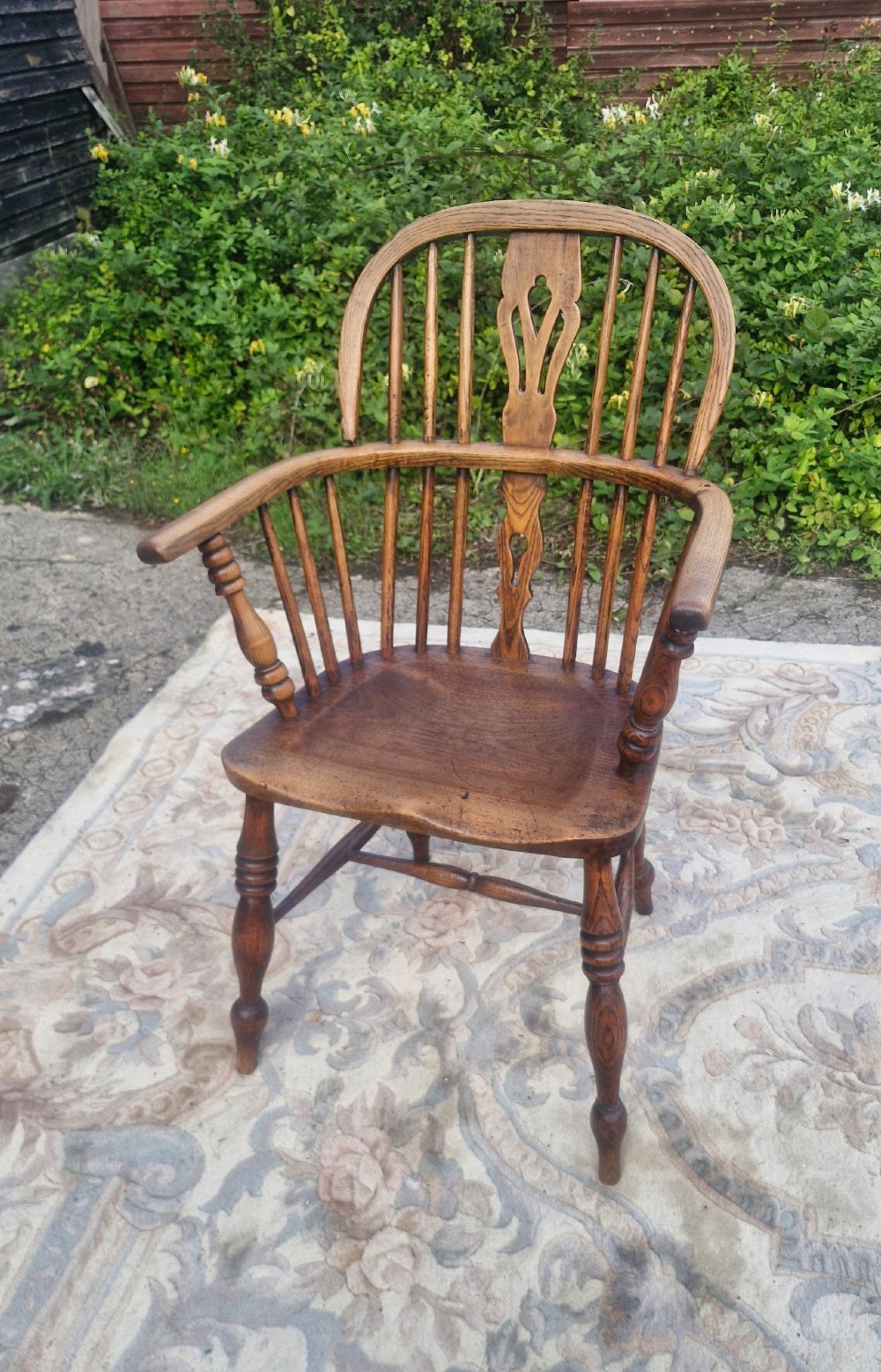 A Victorian wooden Windsor armchair with a bow back, turned spindles, a pierced central splat, integrated armrests, and a contoured saddle seat on turned legs.