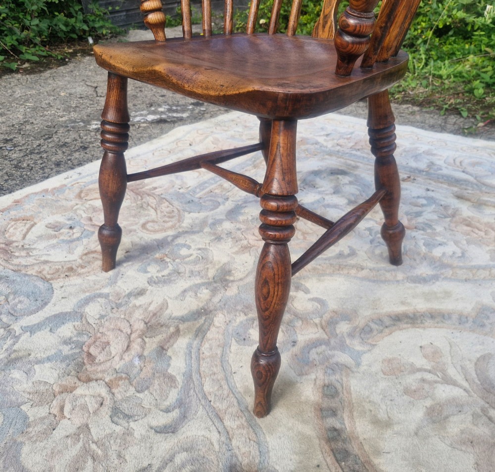 A Victorian wooden Windsor armchair with a bow back, turned spindles, a pierced central splat, integrated armrests, and a contoured saddle seat on turned legs. View III