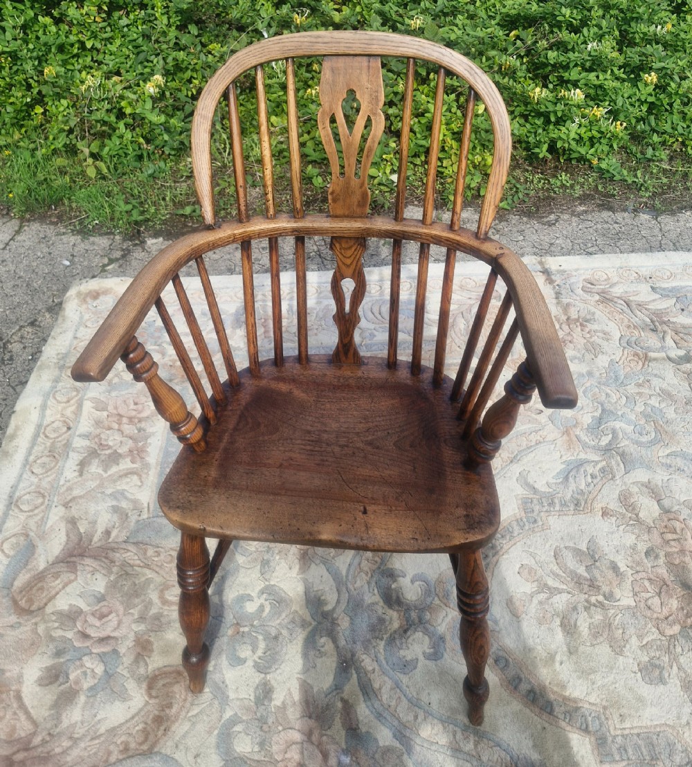 A Victorian wooden Windsor armchair with a bow back, turned spindles, a pierced central splat, integrated armrests, and a contoured saddle seat on turned legs. View V