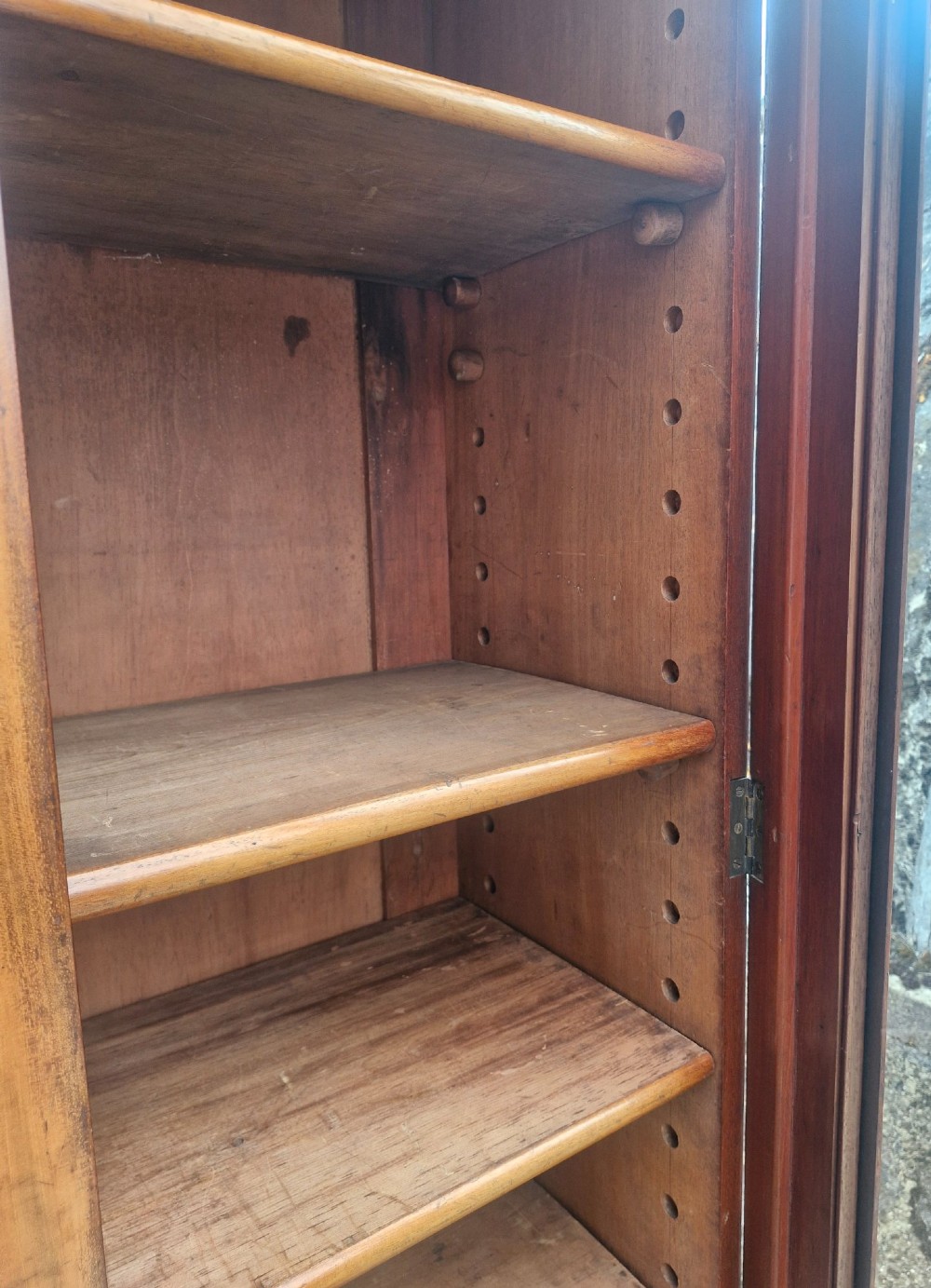 A tall Victorian mahogany bookcase cabinet featuring two arched glazed doors revealing adjustable interior shelving atop a solid plinth base. View II