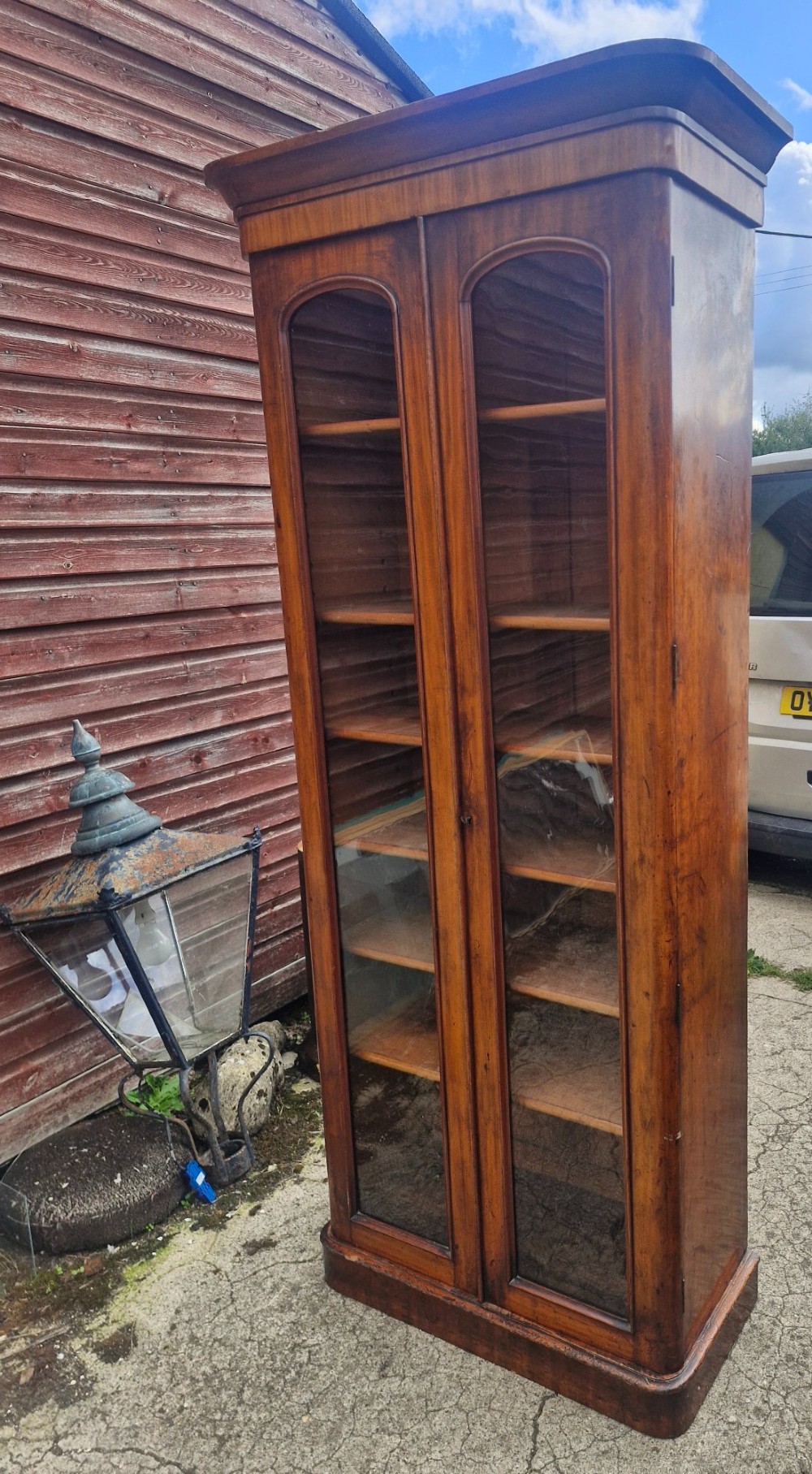 A tall Victorian mahogany bookcase cabinet featuring two arched glazed doors revealing adjustable interior shelving atop a solid plinth base. View IV