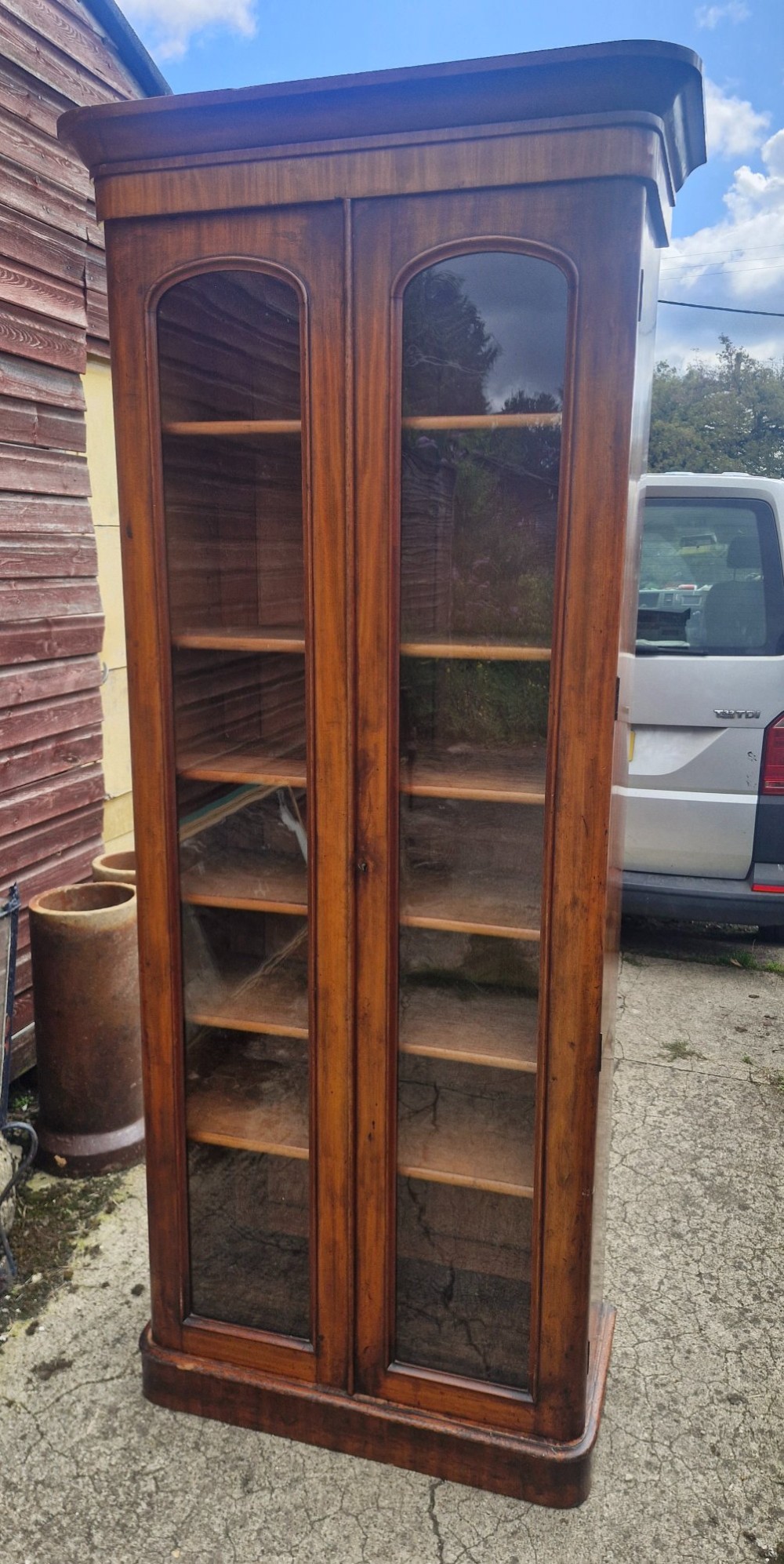 A tall Victorian mahogany bookcase cabinet featuring two arched glazed doors revealing adjustable interior shelving atop a solid plinth base. View V