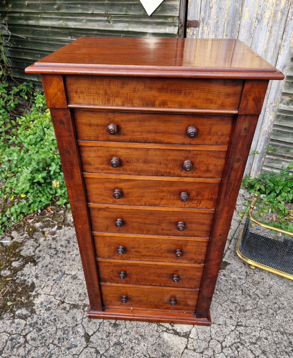A tall Victorian mahogany Wellington chest featuring seven graduated drawers, turned wooden handles, and a hinged side locking flap.